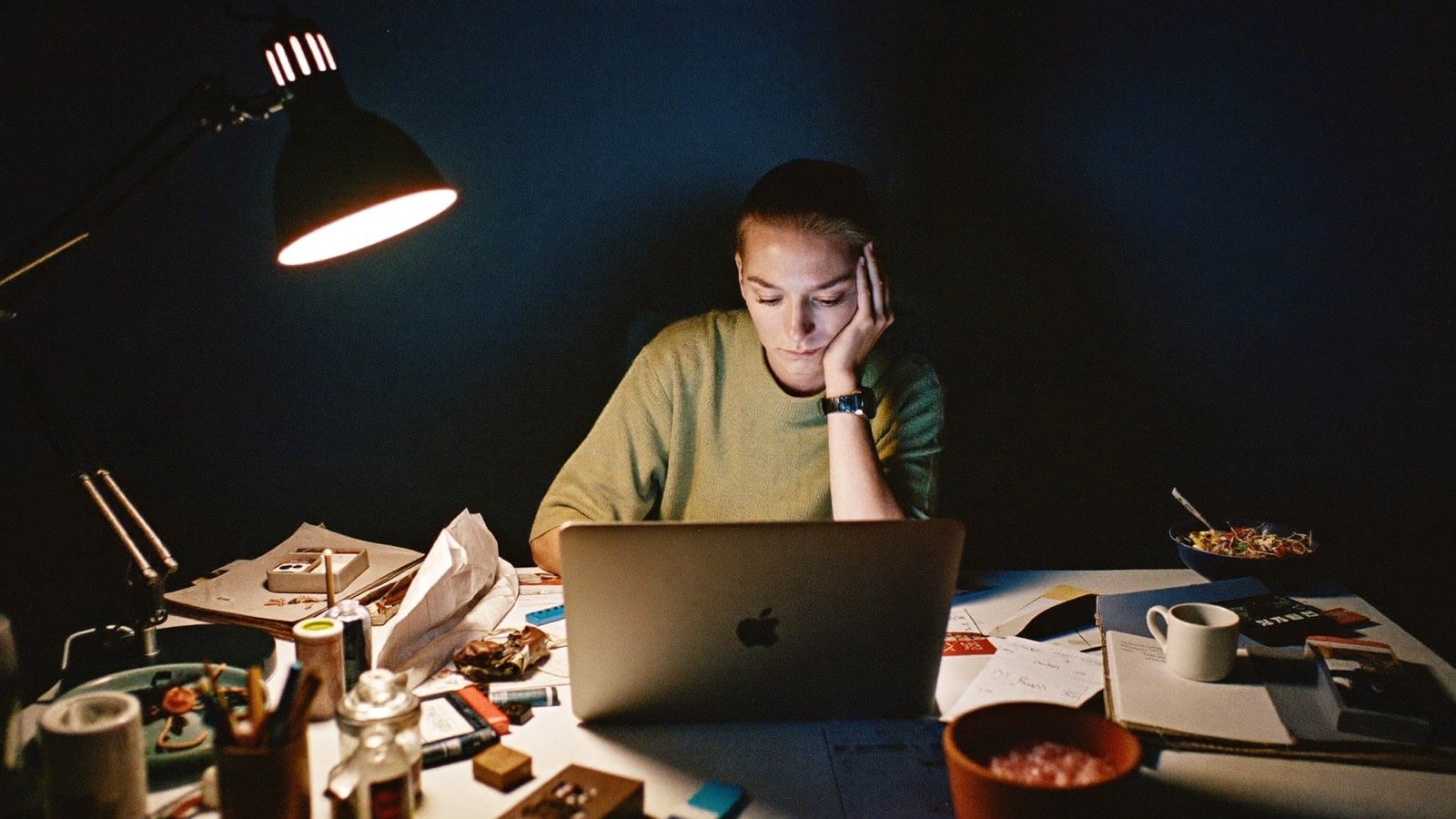A self-employed business owner working late at a cluttered desk, tired in the lamplight